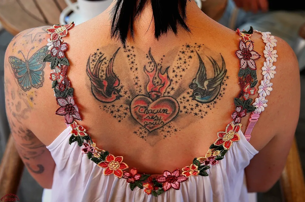 Dos tatoué d'une femme avec un motif d'hirondelles, de fleurs et d'étoiles